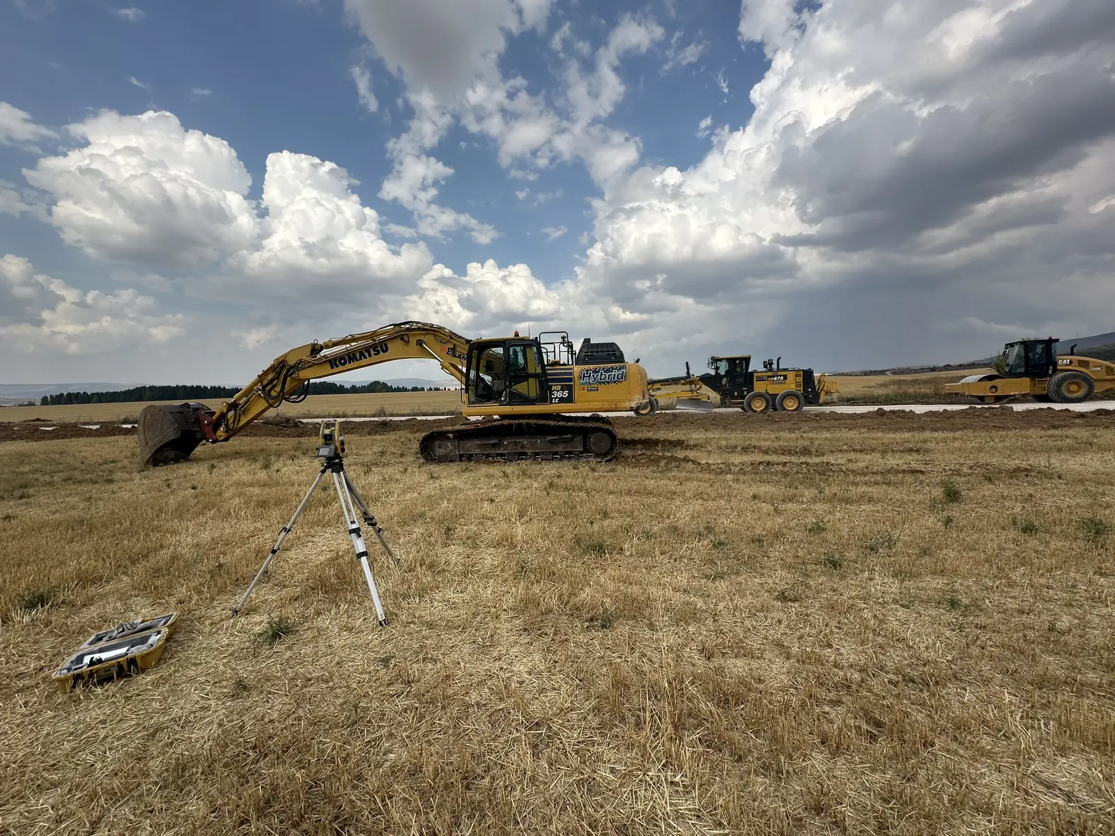 Estación total Topcon en obra junto a una excavadora, una motoniveladora y un compactador